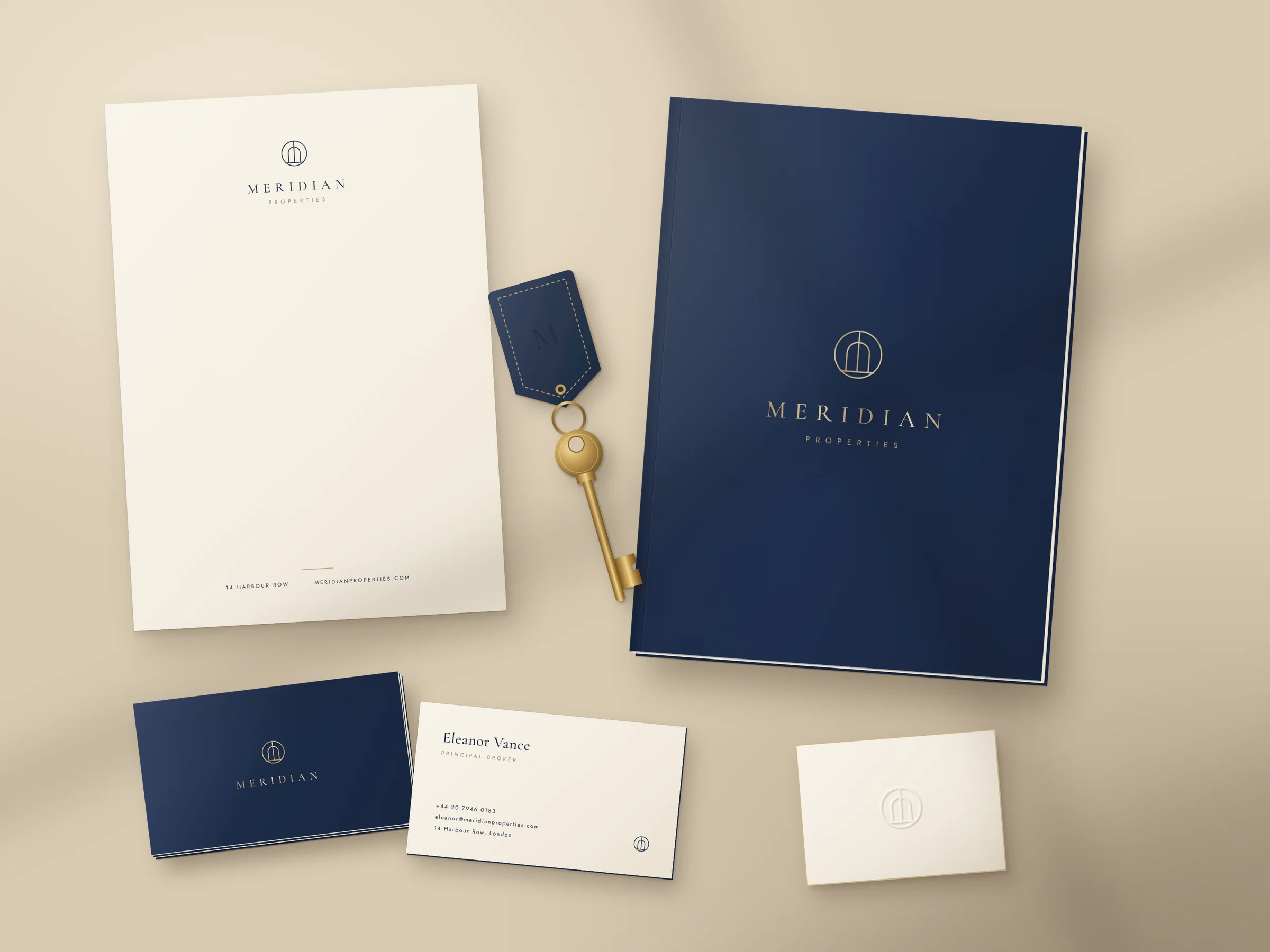 Meridian Properties stationery: cream letterhead, navy presentation folder embossed with the gold mark, business cards for Eleanor Vance, Principal Broker, and a brass key on a navy leather tag.